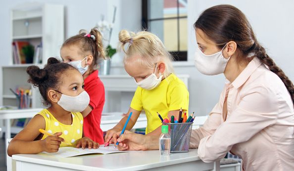 A teacher and children with a mask on their face at school in the classroom after covid19 quarantine and lockdown. Head to head.